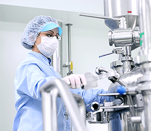 Woman in personal protective equipment handling a machine in a pharma environment.