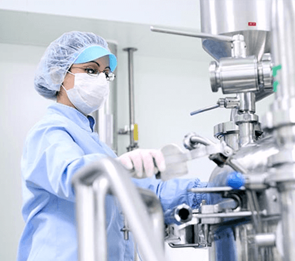 Woman in personal protective equipment handling a machine in a pharma environment.