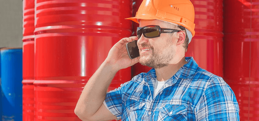 Man with safety helmet on the phone in front of red metal drums.