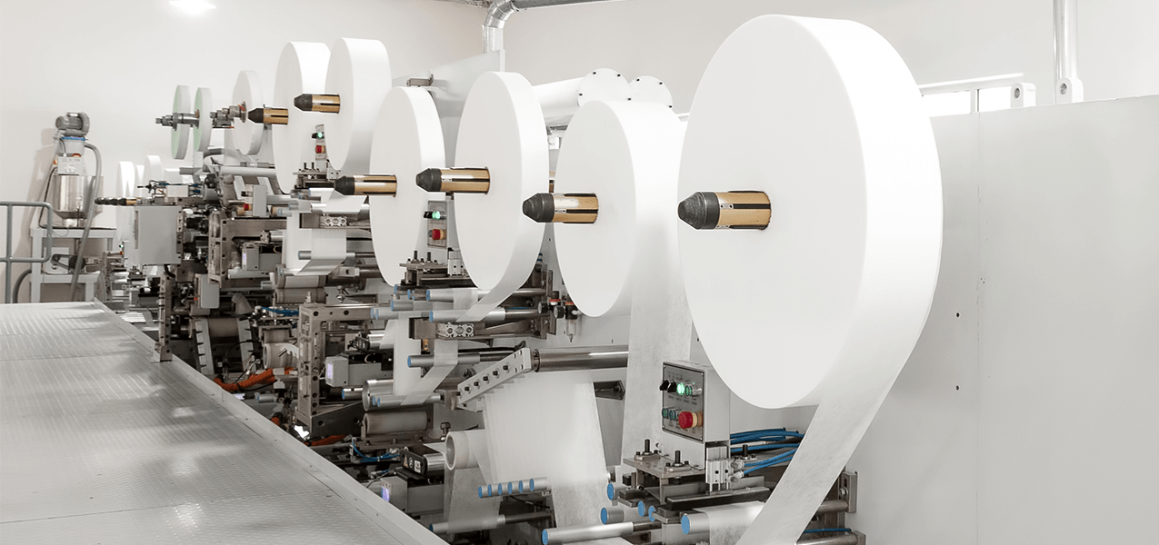 Large machine with many rolls of paper placed on mandrels.