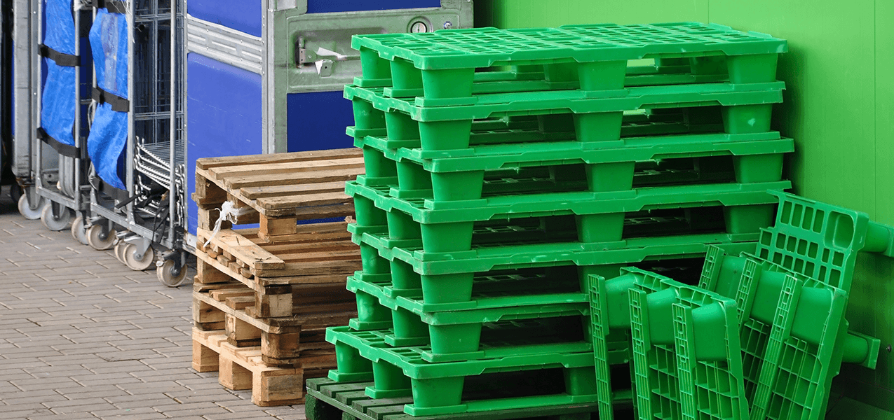 A pile of standard wooden Euro-pallets and a pile of green plastic Euro-pallets.